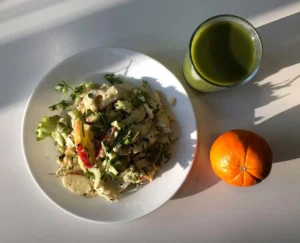 Almás saláta egy fehér tányéron, naranccsal és zöld smoothie-val tálalva a nemsüti kínálatában